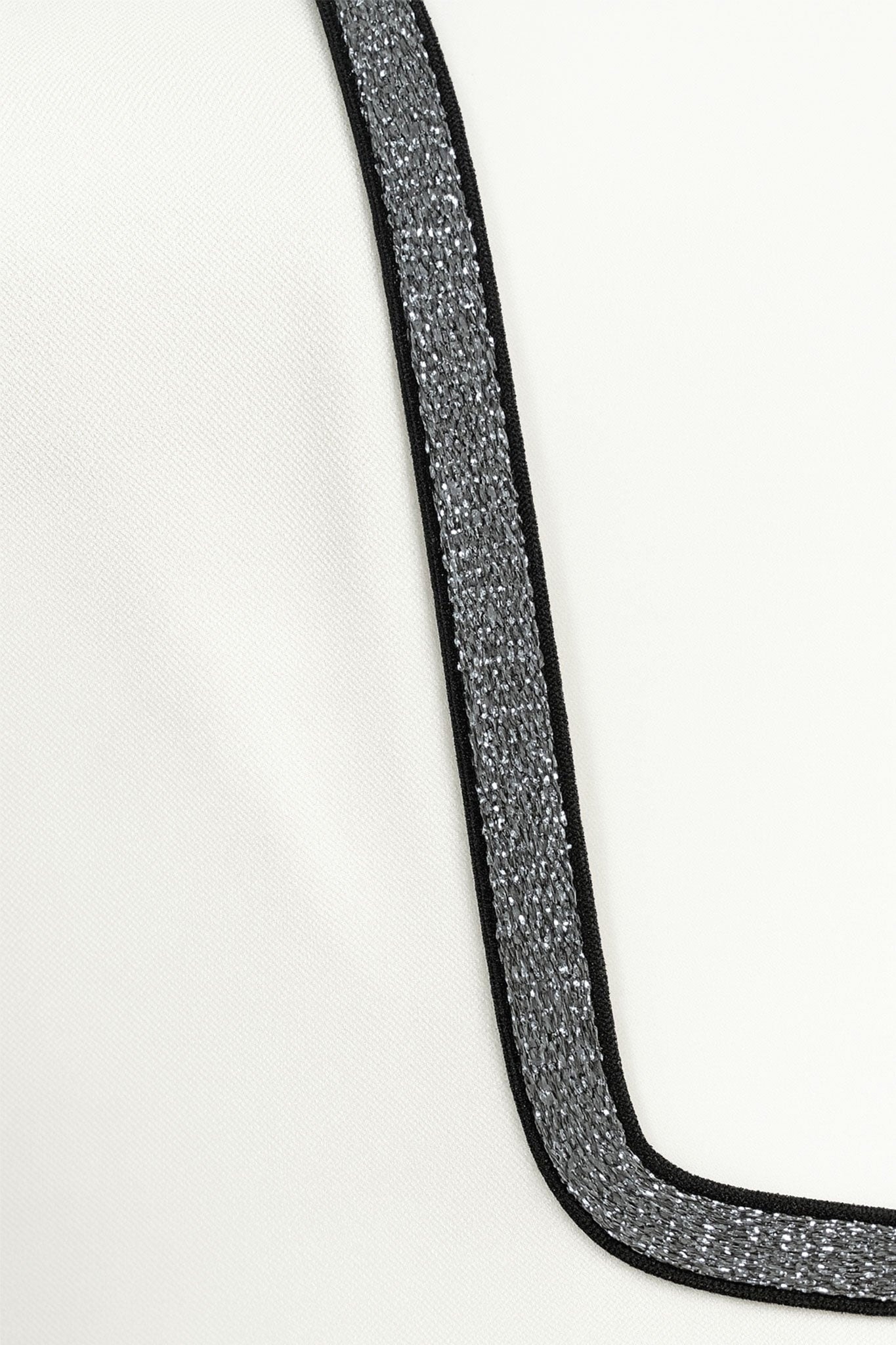 Side detail of the white asymmetric jumpsuit, highlighting the finesse of its chic cut and its colored accent
