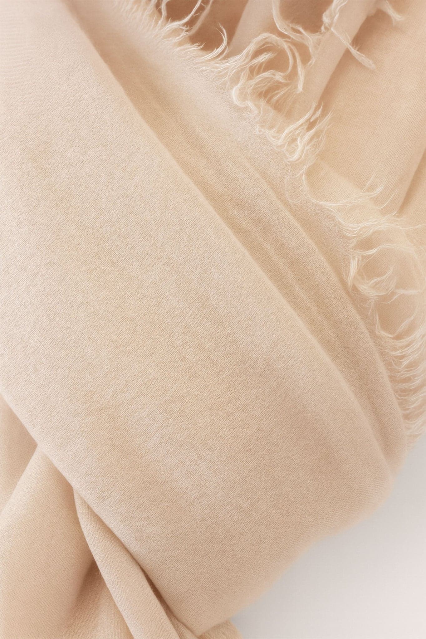 Détail élégant d'une écharpe rose poudré en mélange de modal, laine et cachemire, idéale pour un look raffiné au quotidien.