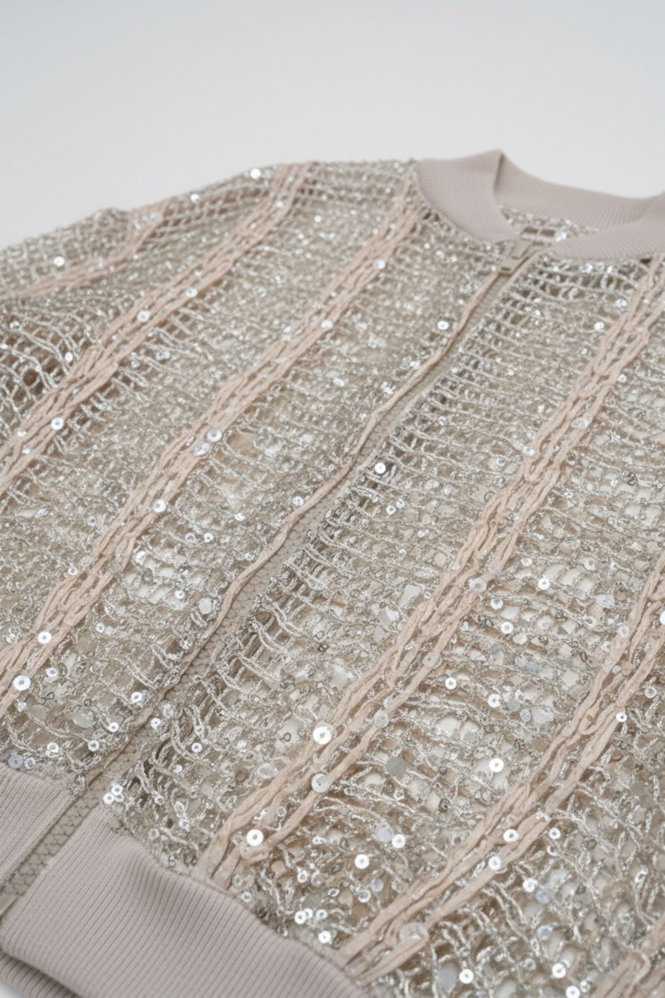 Dettaglio del gilet bomber traforato in lino e seta color champagne, rivelando sequins scintillanti per un look raffinato e...