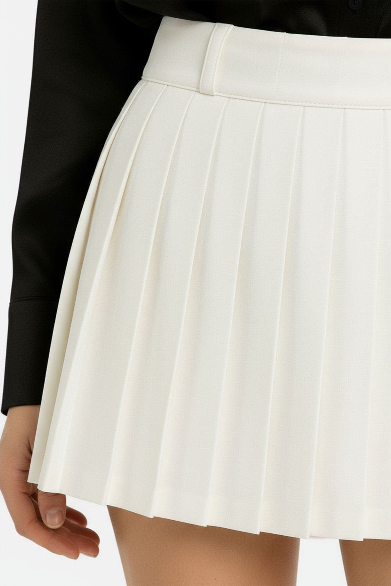 Plis distincts de la jupe courte blanche, soulignant sa coupe fluide et son style élégant pour une tenue de jour raffinée.