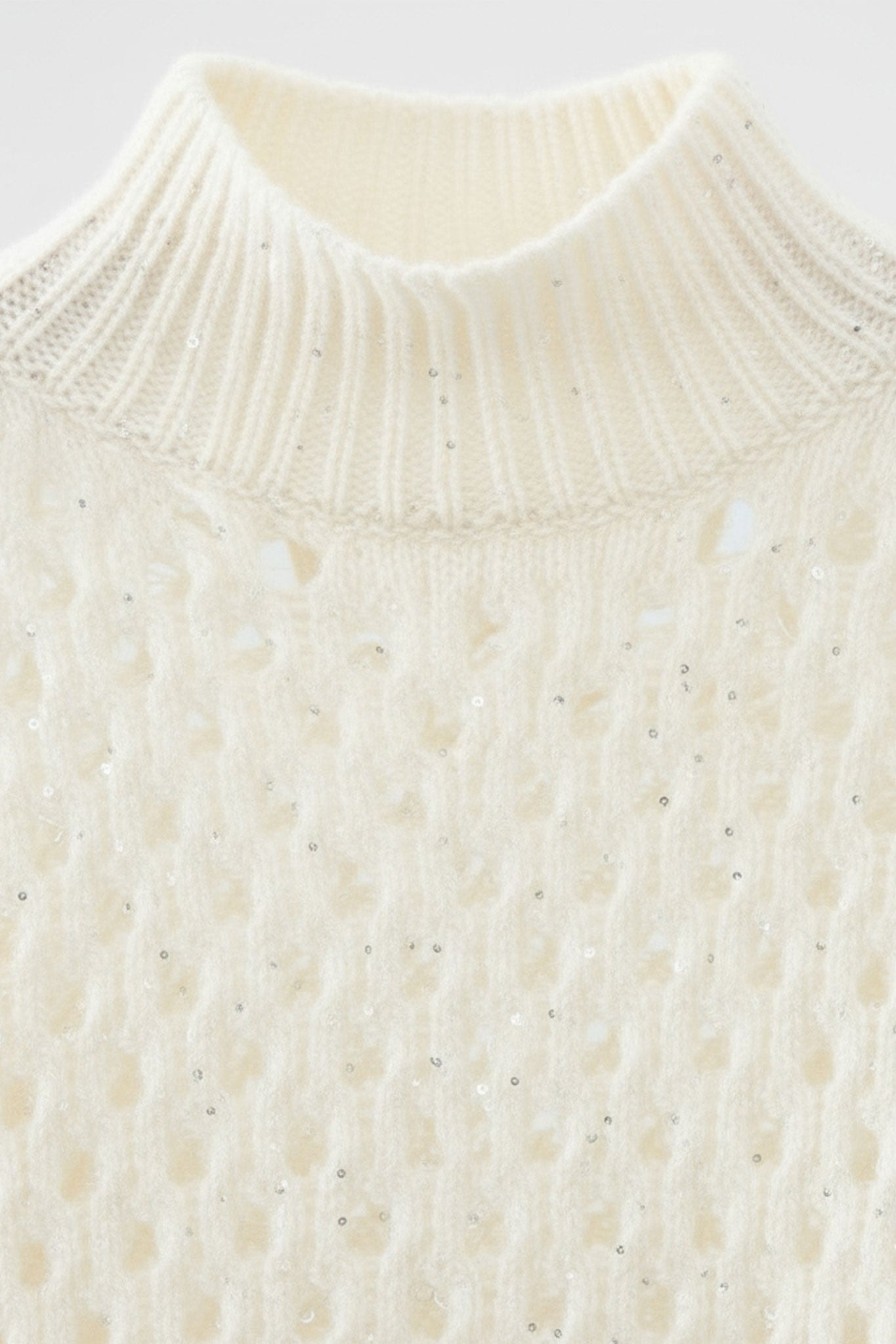 Detail des weißen Lochmuster-Kaschmirpullovers mit Stehkragen, Paillettenverzierungen für einen raffinierten und gemütlichen Look.