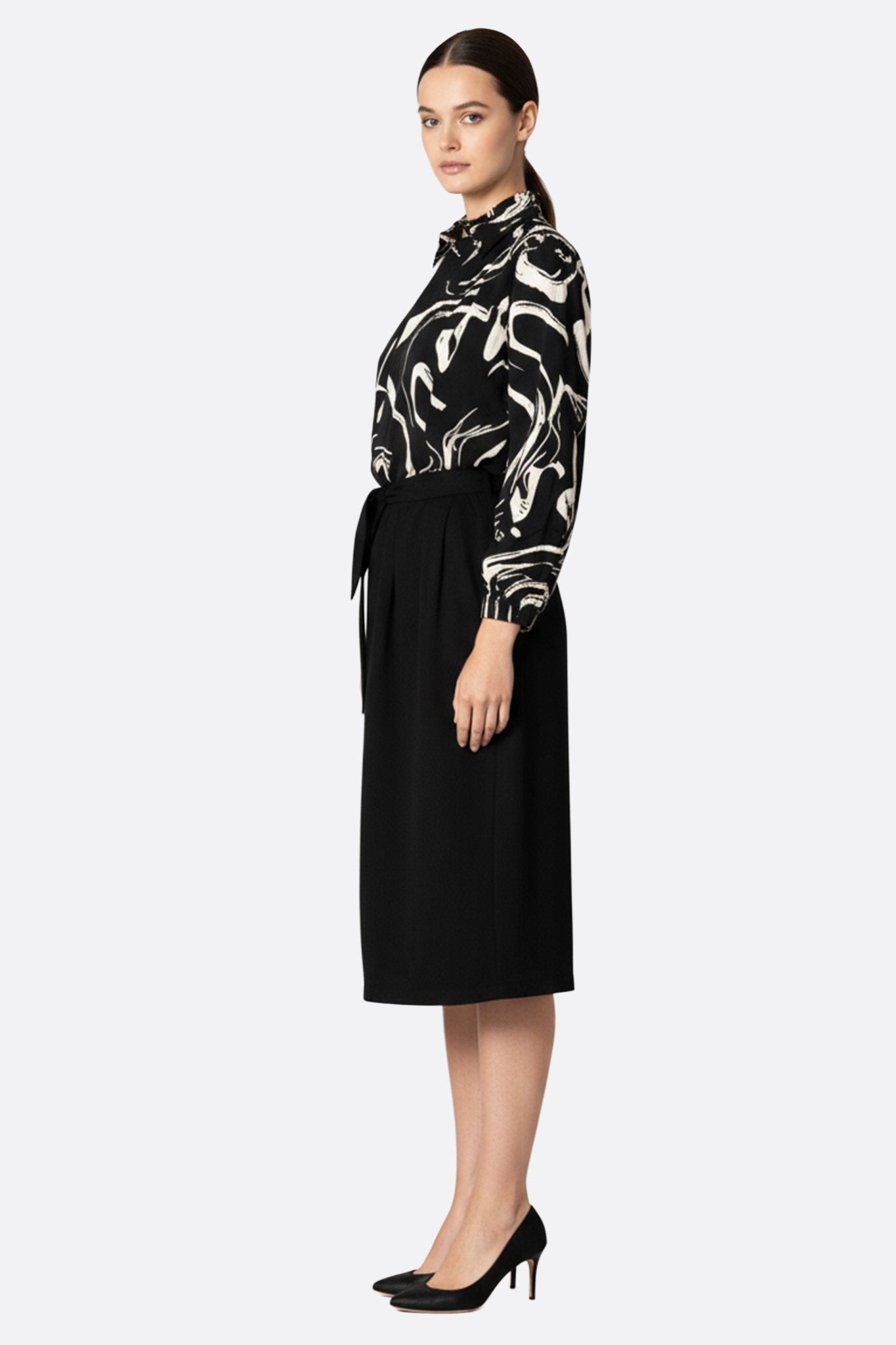 Détail élégant de la robe mi-longue noire avec ceinture nouée et haut imprimé artistique pour une allure raffinée.