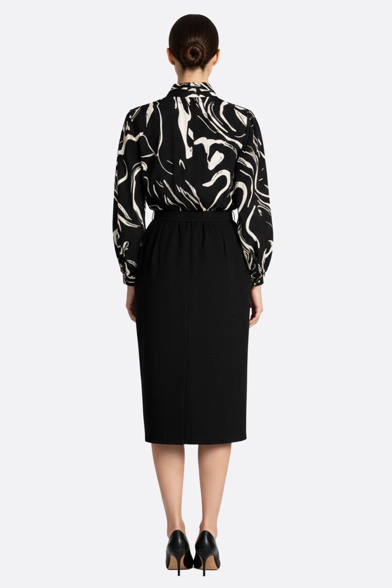 Robe mi-longue noire à ceinture nouée, mettant en valeur son haut à imprimé artistique dans un angle 3/4 élégant.