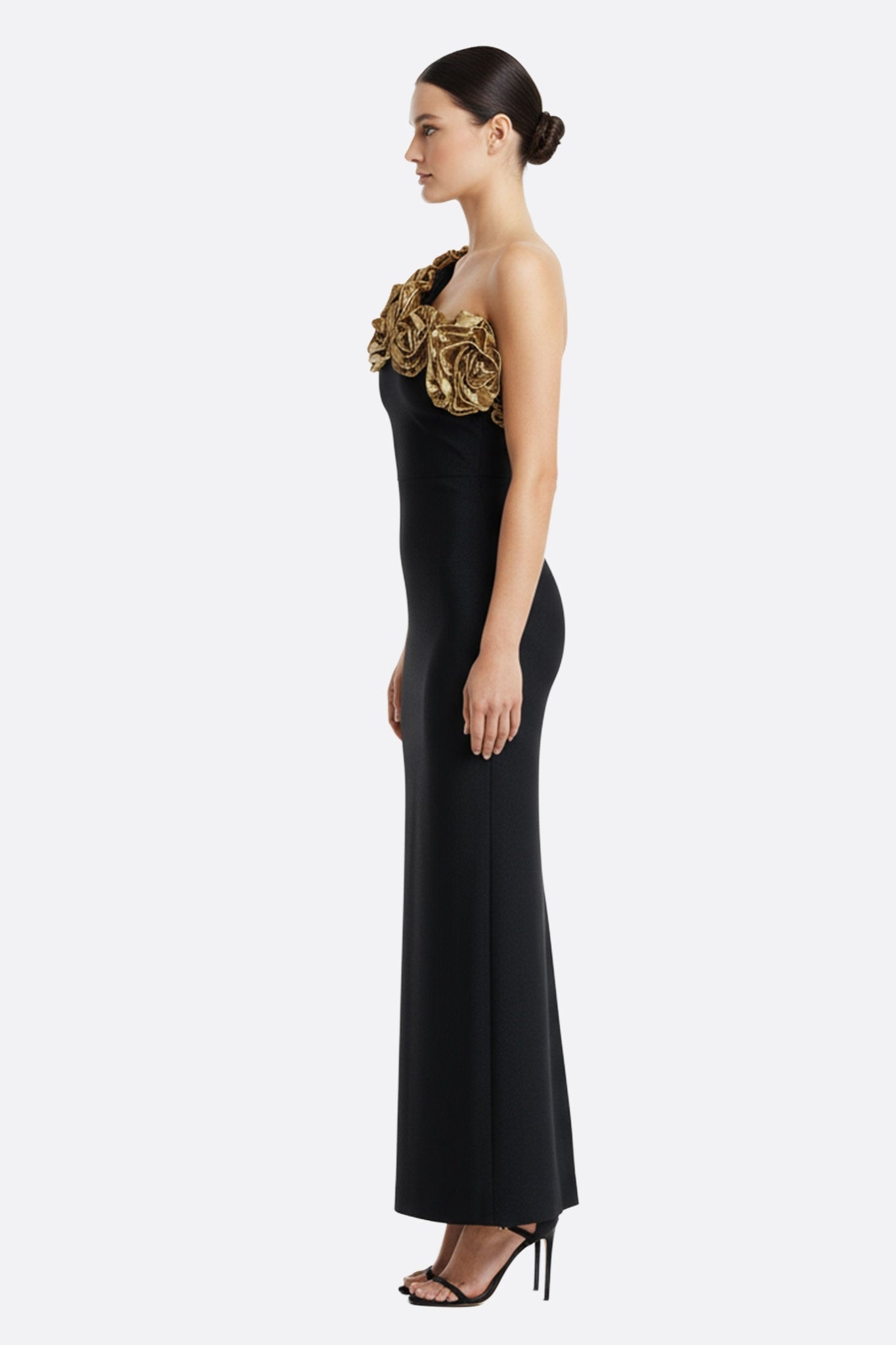 Détail de la robe noire à encolure asymétrique, mettant en valeur ses fleurs dorées pour une allure chic et raffinée.