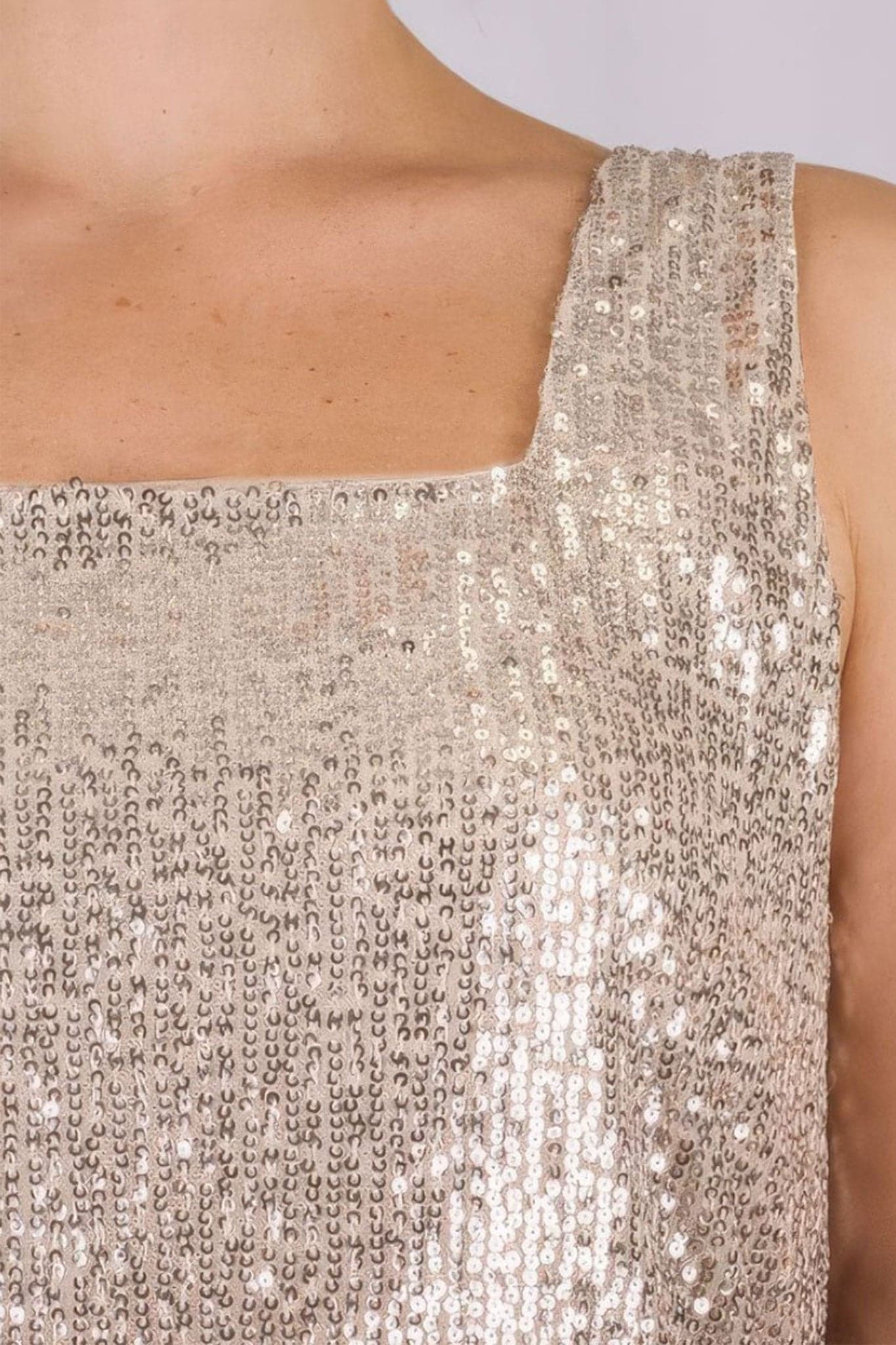 Détail du top beige à sequins irisés, mettant en valeur sa texture fluide et son charme élégant pour soirées glamour.