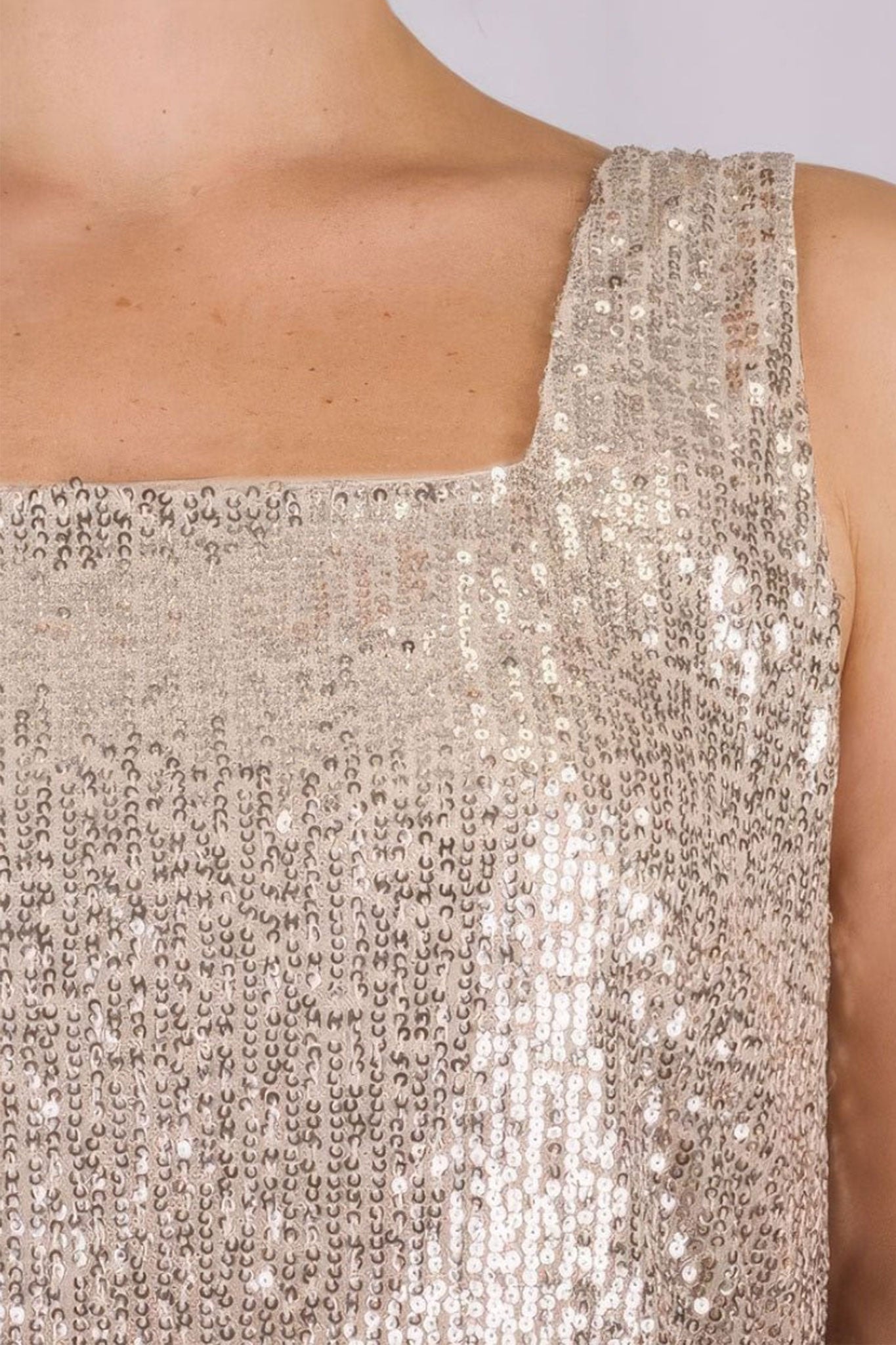 Détail du top beige à sequins irisés, mettant en valeur sa texture fluide et son charme élégant pour soirées glamour.