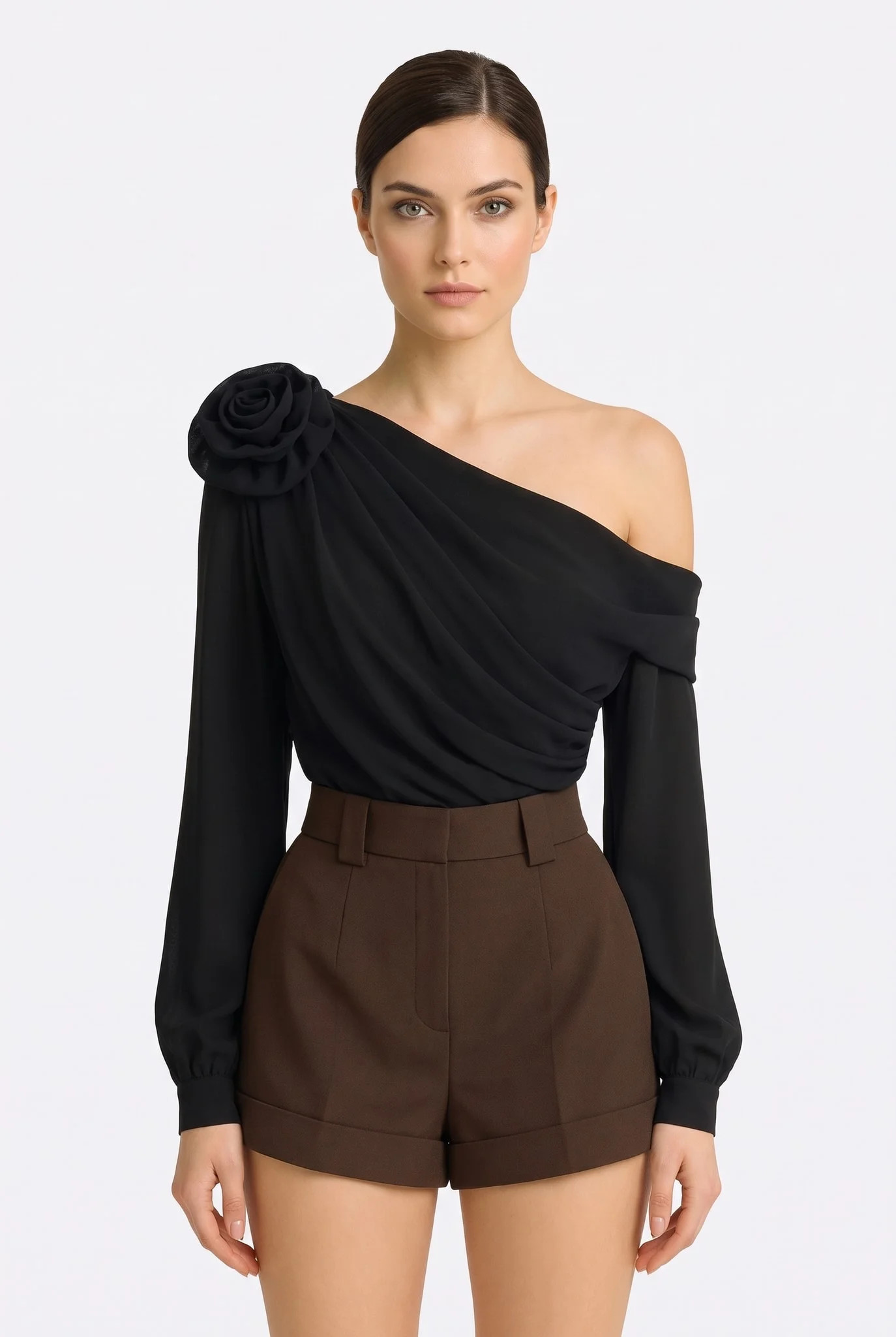 Mannequin de face portant le top asymétrique noir drapé à fleur sculptée, épaule dénudée et manches longues